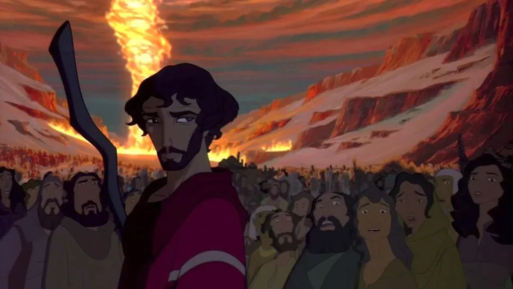 A still from the animated film “The Prince of Egypt” (1996), capturing a powerful and dramatic moment. The central character, a bearded man in a red tunic, holds up a staff against a backdrop of a massive fiery tornado, or “a pillar of fire.” His expression is serious and determined, reflecting the gravity of the scene. Behind him, a diverse crowd of onlookers, depicted with varying expressions of awe and fear, watch the spectacle unfold.